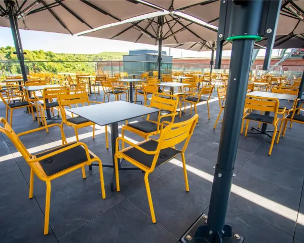 Leere gelbe Stühle und Tische unter Sonnenschirmen auf der Terrasse des Zeche Ewald Cafés.