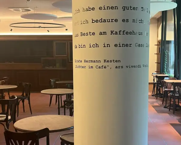 Gemütliches **cafe vegan** mit vielen Tischen und Stühlen. Eine Säule ziert ein Zitat von Hermann Kesten über das Kaffeehaus.