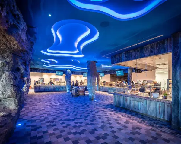 Einzigartiges Ambiente im Rulantica Essen: Wasserfall, Felsen und blaue Wellen beleuchten die Essensausgabe.