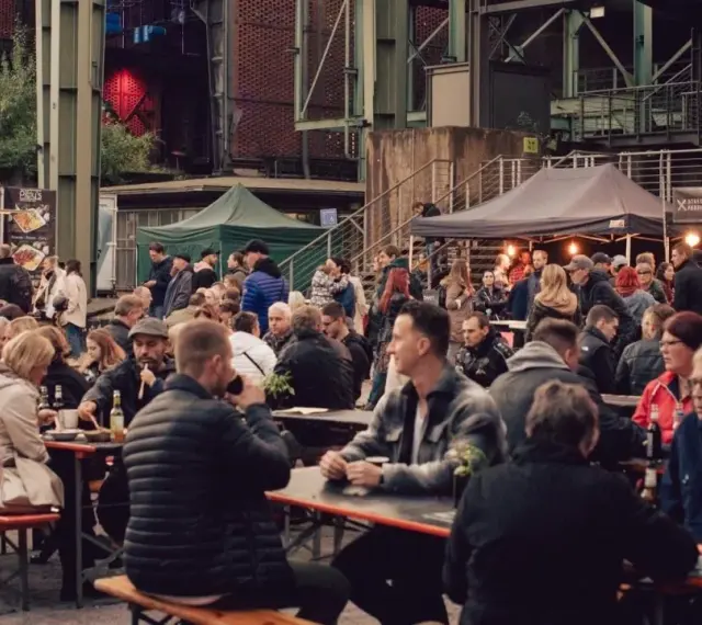 Menschen genießen Speisen und Getränke auf dem Street Food Festival Duisburg. Viele Besucher sitzen an langen Tischen und unter Zelten.