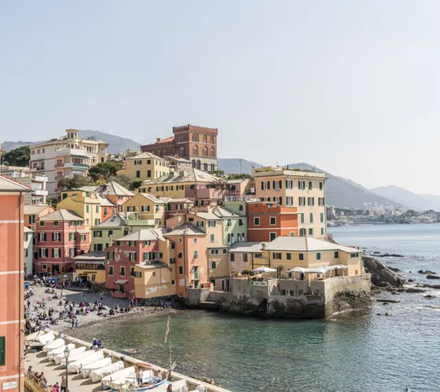 Bunte Häuserfronten am Meer in Genua, Italien. Boote liegen am Ufer, Menschen entspannen sich am Strand.