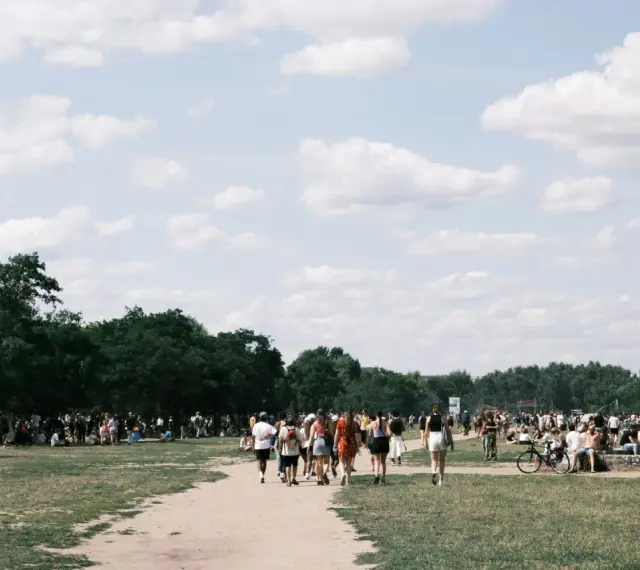 Menschen strömen über eine Wiese, unter Bäumen und Zelten. Ein sonniger Tag, wo ist Pfingsten was los?