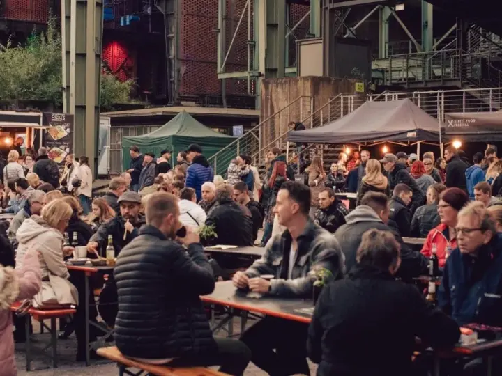 Menschen genießen Speisen und Getränke auf dem Street Food Festival Duisburg. Viele Besucher sitzen an langen Tischen und unter Zelten.