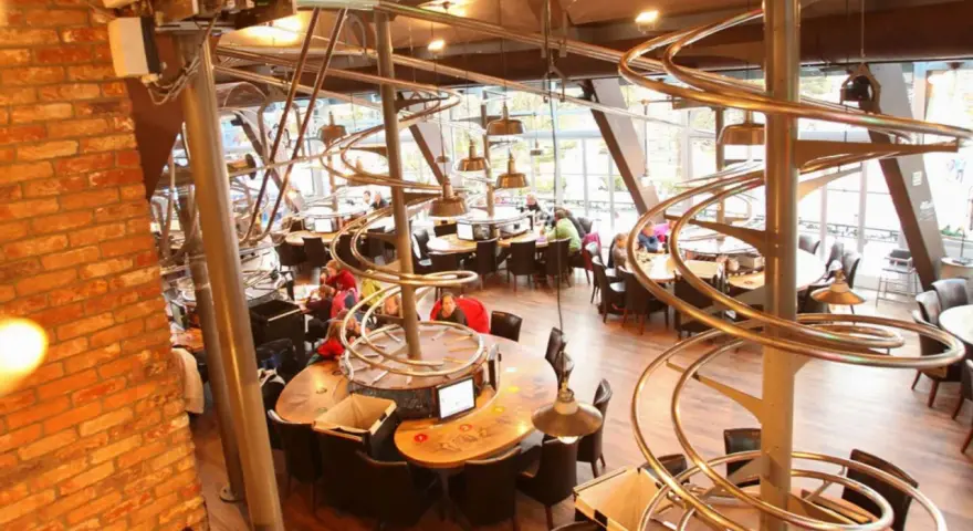 Einzigartiges Restaurant im Europa-Park mit Achterbahn-Schienen als Deko. Gäste sitzen an runden Tischen unter den metallischen Kurven.