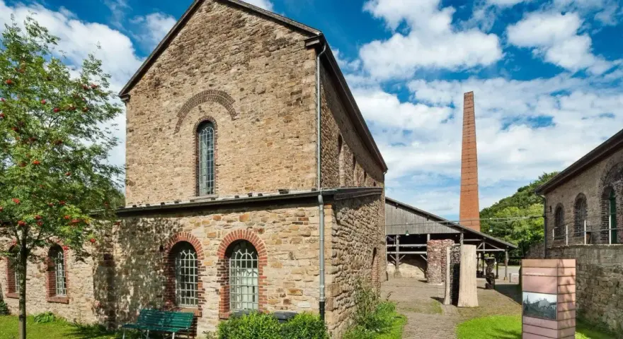Altes rheinisches Bergwerk mit Backsteinkamin und einem Baum mit roten Beeren.