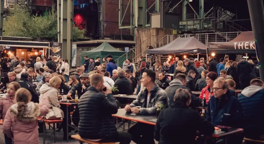 Menschen genießen Speisen und Getränke auf dem Street Food Festival Duisburg. Viele Besucher sitzen an langen Tischen und unter Zelten.