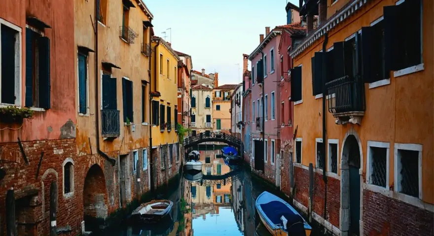 Bunte Häuser säumen einen Kanal in Venedig. Kleine Boote treiben auf dem Wasser. Ein kleiner Bogenbrücke überspannt den Kanal. Das ist, was man in Venedig gesehen haben muss.