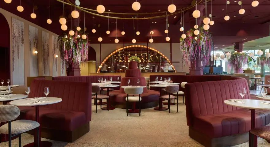 Efteling restaurant mit roten Samt-Sitzbänken, runden Marmortischen und üppigen Blumenarrangements. Hängende Kugelleuchten schaffen eine warme Atmosphäre.