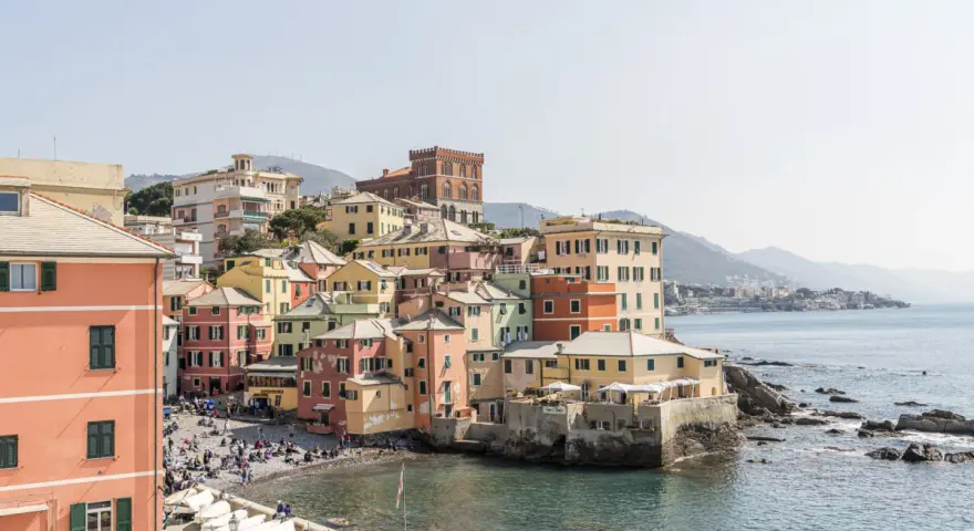 Bunte Häuserfronten am Meer in Genua, Italien. Boote liegen am Ufer, Menschen entspannen sich am Strand.