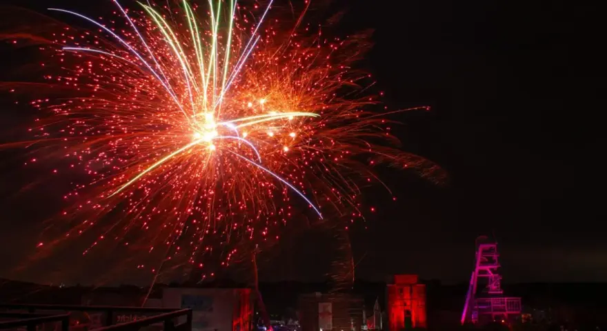 Feuerwerk über Herten: Ein Spektakel, das an eine Extraschicht der Freude erinnert. Rote und gelbe Funken sprühen, während ein Förderturm in Pink leuchtet.
