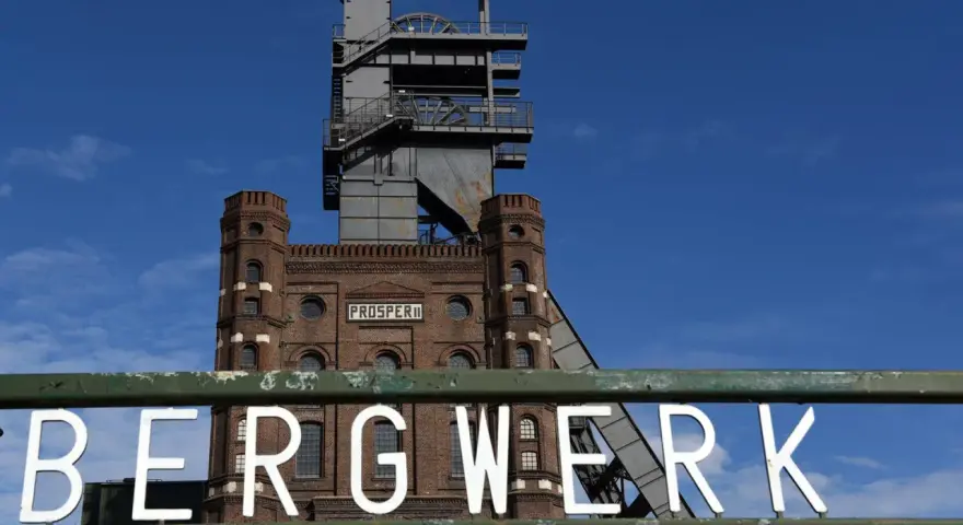 Das alte Bergwerk Prosper Haniel mit seinem markanten Förderturm ragt gegen einen blauen Himmel auf.