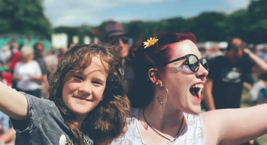 Zwei lachende Frauen, eine davon ein Kind, genießen das vivawest family festival. Glitzer auf den Wangen und eine Blume im Haar.