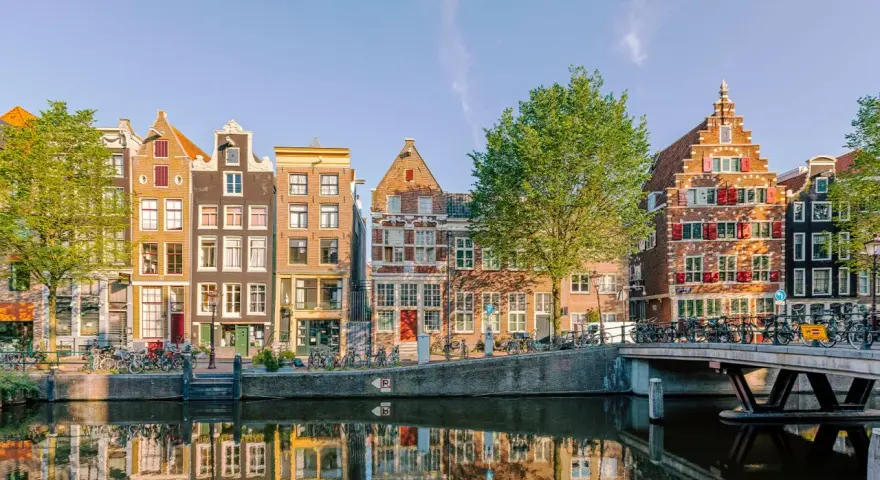 Bunte Grachtenhäuser spiegeln sich im Wasser. Fahrräder säumen den Kanal. So viel **was kann man in Amsterdam machen**!