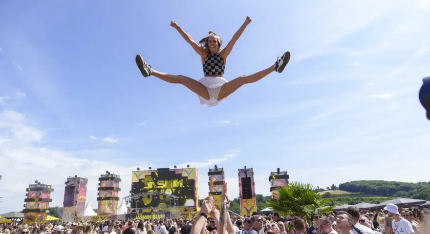 Eine Frau macht einen Spagat in der Luft vor einer Bühne bei einem der Festivals NRW. Die Menge jubelt.