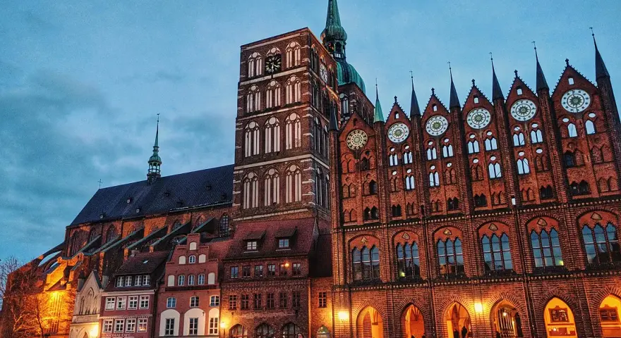 Abendstimmung auf dem Marktplatz der **Stralsund Altstadt**. Backsteingotik dominiert, mit dem Rathaus und der Marienkirche im Dämmerlicht.
