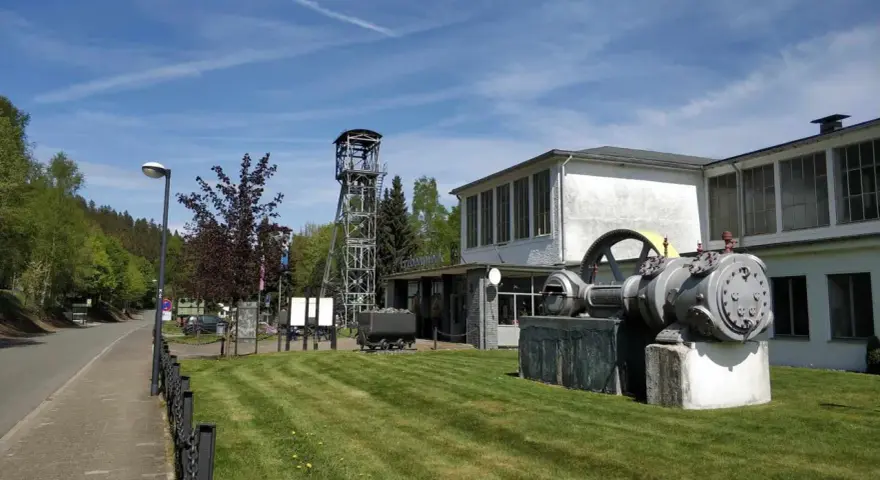 Ein historisches Bergwerk lädt zum Bergwerk besichtigen ein. Eine Förderturmanlage und alte Maschinen stehen vor dem Gebäude.