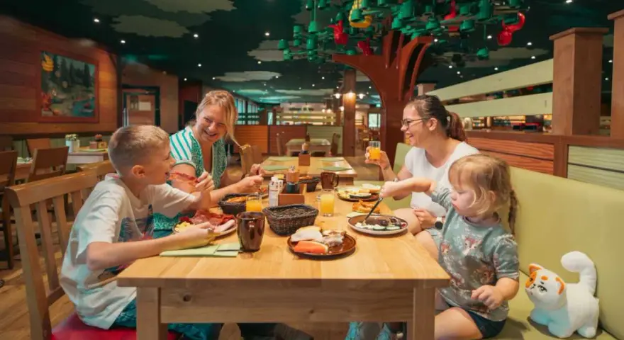 Familie genießt ein fröhliches Frühstück in einem fantasievollen Legoland Restaurant mit Baumdeko.
