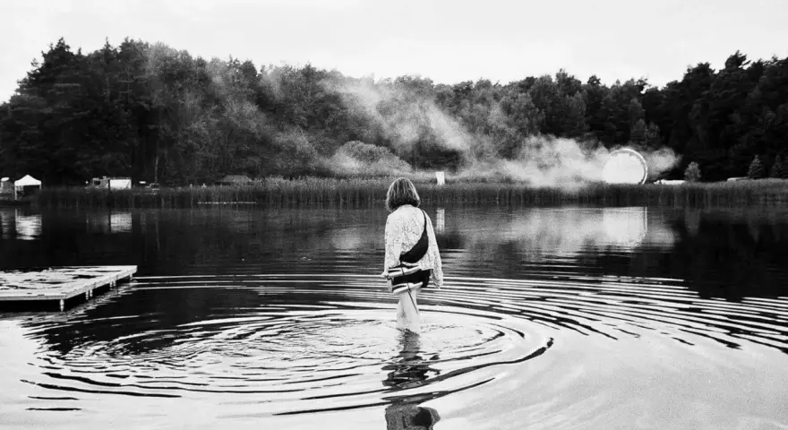 Ein Mädchen watet im Wasser, während im Hintergrund Nebel und eine Lichtinstallation zu sehen sind. Ein friedlicher Moment beim nachtigall festival.