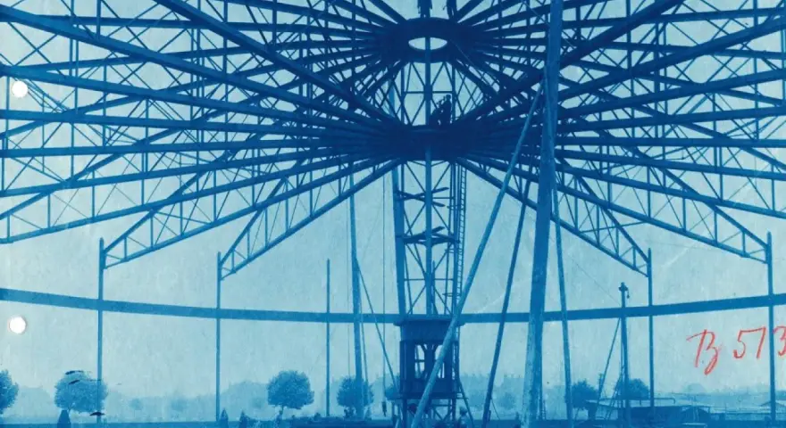 Bau des Riesenrades am GHH Oberhausen. Die Stahlkonstruktion ragt in den Himmel, Arbeiter sind auf der Spitze zu sehen.