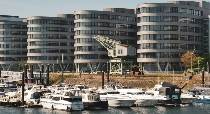 Moderne Gebäude am Duisburg Innenhafen mit vielen Yachten im Wasser. Ein alter Kran erinnert an die industrielle Vergangenheit.