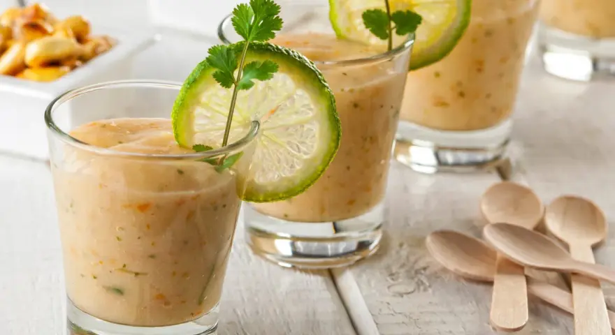 Erfrischende Gläser mit cremiger Tigermilch, garniert mit Limettenscheiben und Koriander. Kleine Holzlöffel liegen bereit.