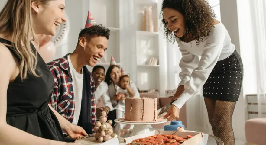 Fröhliche Gruppe feiert den 30. Geburtstag mit Kuchen und Keksen. Alle tragen Partyhüte und lachen ausgelassen.