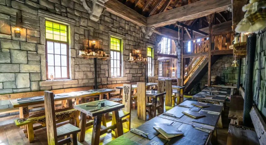 Rustikale Phantasialand Taverne mit Steinwänden, Holztischen und Bänken, Kerzenlicht und mittelalterlichem Flair.