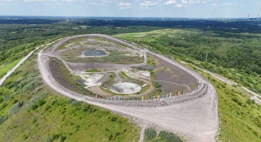 Die Halde Haniel mit ihrem Amphitheater und bunten Stelen, umgeben von grüner Natur und Windrädern in der Ferne.