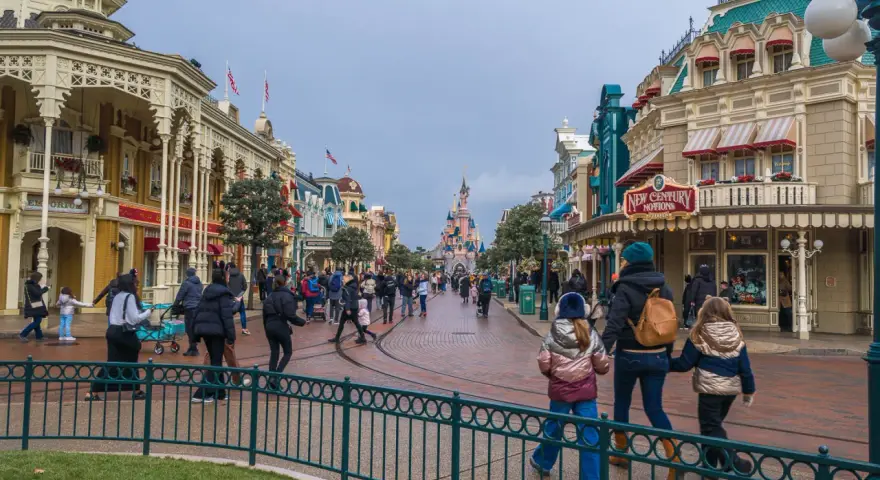 Menschen schlendern die Hauptstraße entlang, vorbei an Geschäften und dem Schloss. Ein Tag im Disneyland, vielleicht mit einem Disneyland Fastpass für die Attraktionen.