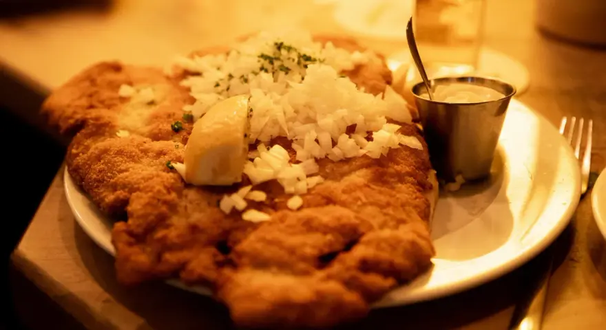 Ein knuspriges Schnitzel mit Zwiebeln und Zitrone, wie bei Oma Kleinmanns. Dazu ein Dip und ein Glas Wasser.