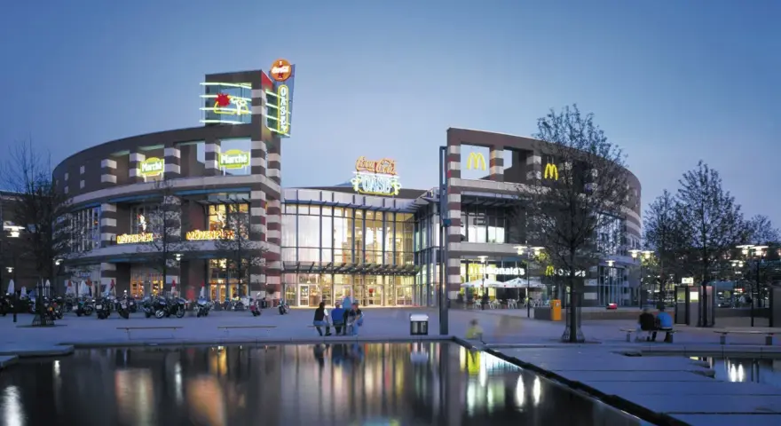 Abendstimmung am Centro Oberhausen. Die beleuchtete Fassade mit den Logos von McDonald's und Coca-Cola spiegelt sich im Wasser.