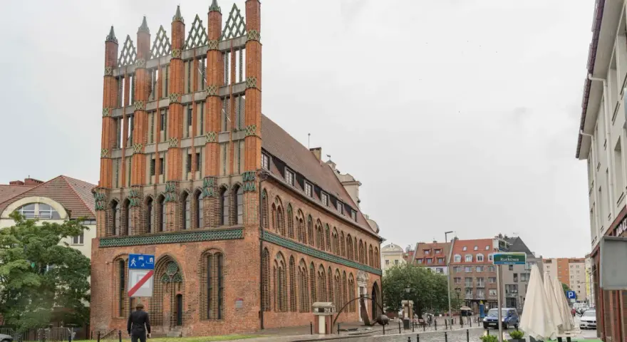 Ein Mann geht durch die regennasse **Stettin Altstadt** an einem Backsteingebäude mit Spitzdächern vorbei.