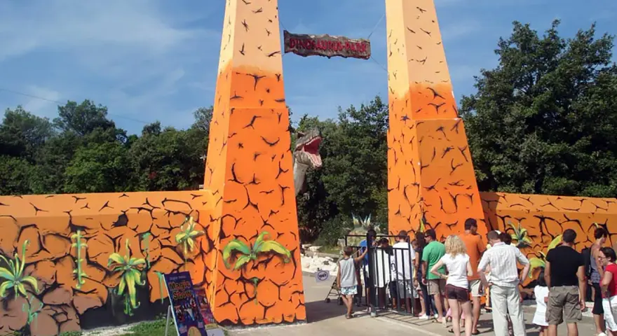 Eingang zum Dinosaurier-Park, einem Freizeitpark in Kroatien. Eine Gruppe von Besuchern steht vor dem Eingangstor.