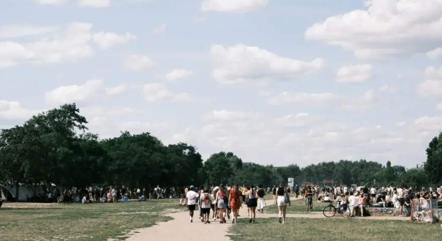 Menschen strömen über eine Wiese, unter Bäumen und Zelten. Ein sonniger Tag, wo ist Pfingsten was los?