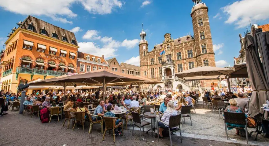Lebhafter venlo markt mit vielen Menschen, die in Cafés unter Sonnenschirmen sitzen. Im Hintergrund das historische Rathaus.