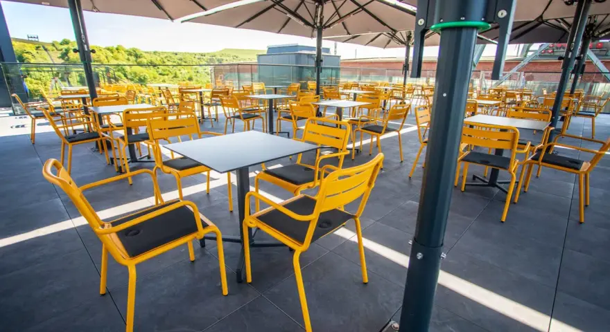Leere gelbe Stühle und Tische unter Sonnenschirmen auf der Terrasse des Zeche Ewald Cafés.