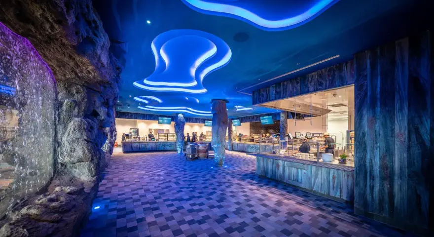 Einzigartiges Ambiente im Rulantica Essen: Wasserfall, Felsen und blaue Wellen beleuchten die Essensausgabe.