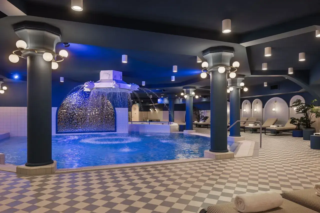 Ein luxuriöses Efteling Schwimmbad mit blauer Beleuchtung, einem Wasserfall und Liegestühlen.
