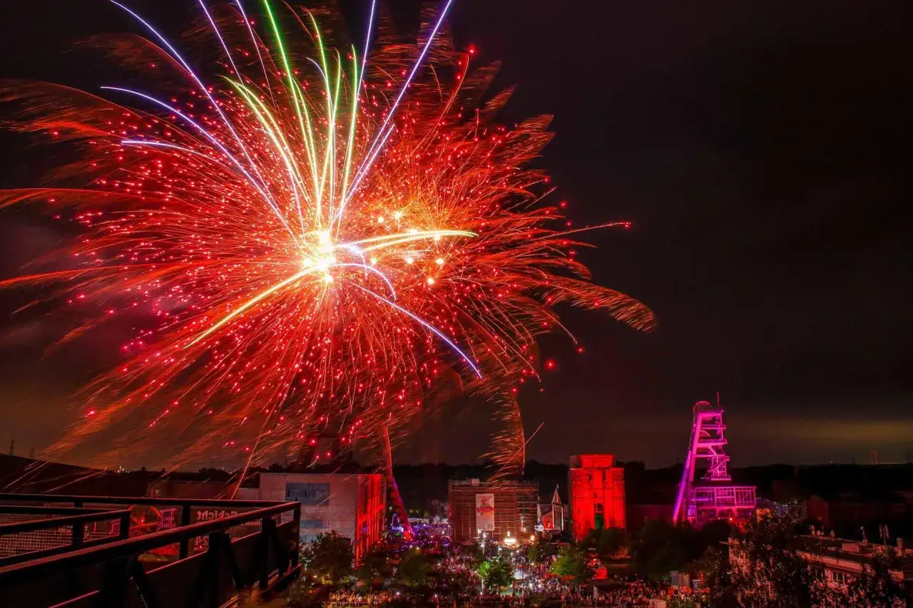 Feuerwerk &uuml;ber Herten: Ein farbenpr&auml;chtiges Spektakel erhellt den Nachthimmel, w&auml;hrend unten Menschenmassen feiern. Die Zeche ist beleuchtet, ein besonderes Highlight f&uuml;r die Extraschicht Herten.