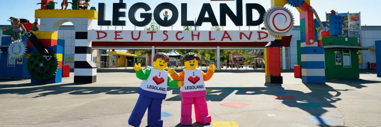 Zwei Lego-Figuren begrüßen Besucher vor dem Legoland Deutschland. Die Attraktion ist an Wochentagen oft weniger überlaufen.