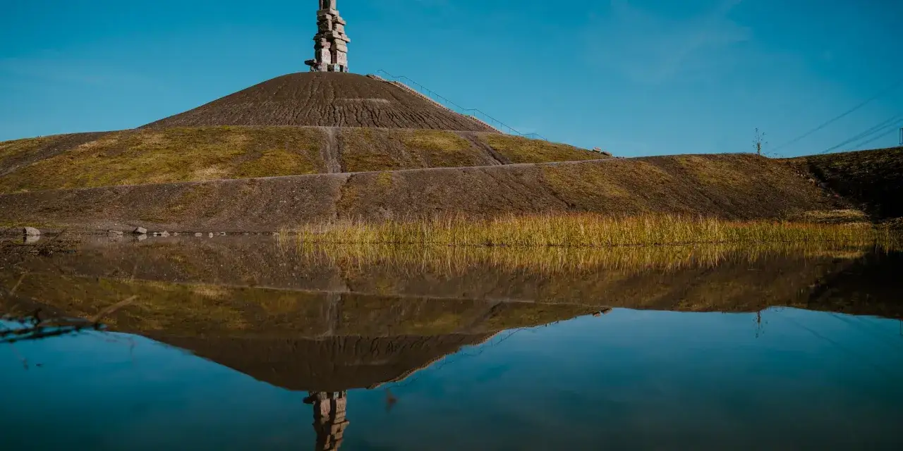 Die Halde Rheinelbe, eine k&uuml;nstliche Berglandschaft, spiegelt sich im ruhigen Wasser.