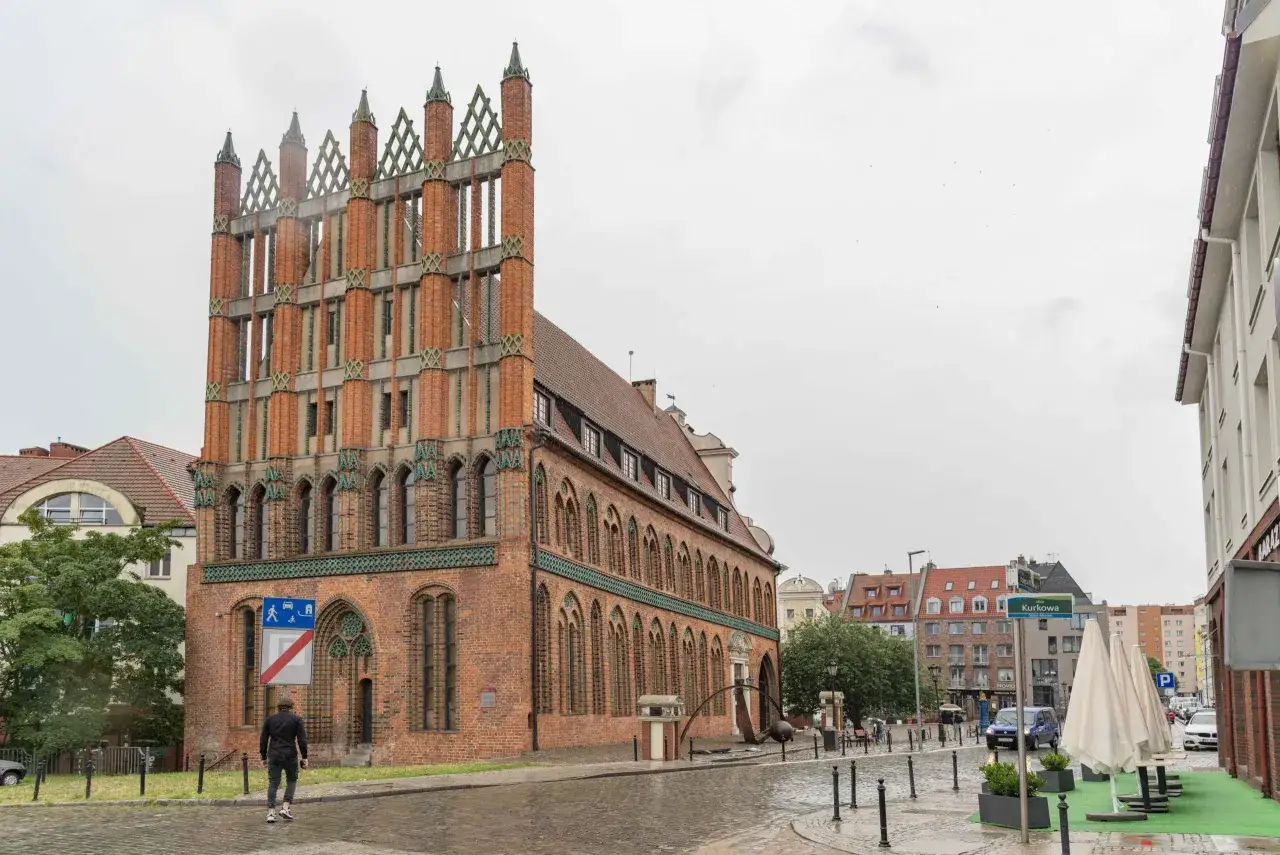 Ein Mann geht durch die regennasse Stettin Altstadt an einem Backsteingebäude mit Spitzdächern vorbei.