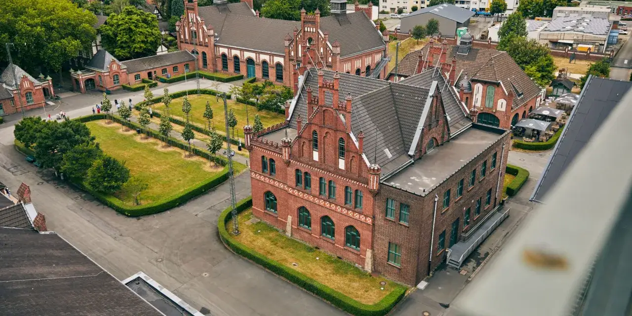 Historische Backsteingeb&auml;ude des Zollern-Kraftwerks mit begr&uuml;nten Innenh&ouml;fen und B&auml;umen.