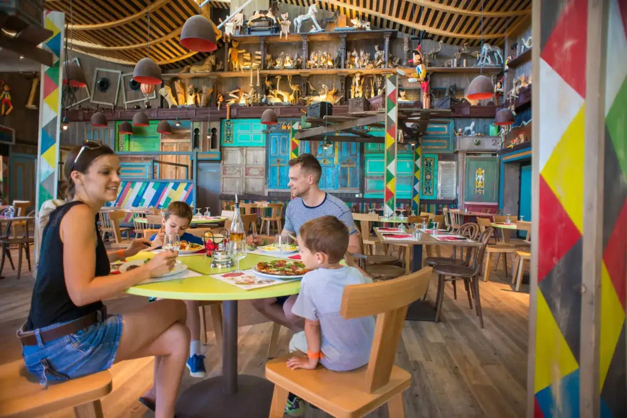 Familie genießt Pizza in einem bunten Center Parcs Restaurant mit vielen Dekorationen an den Wänden.