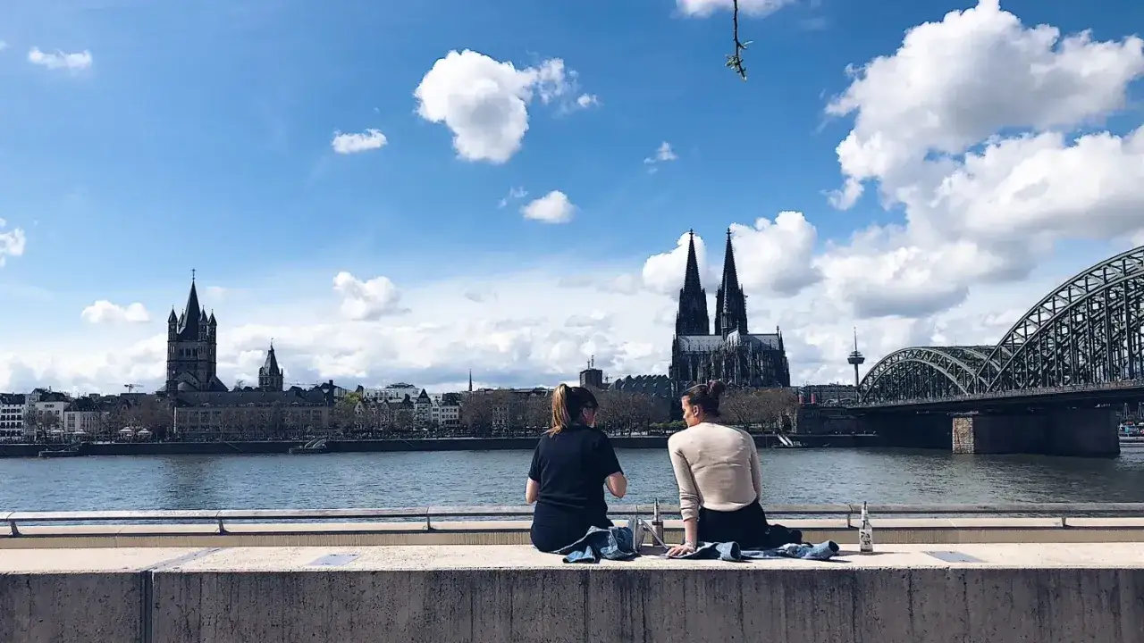 Zwei Frauen genie&szlig;en den Ausblick auf die K&ouml;lner Skyline von einer Rooftop Bar. Dom und Hohenzollernbr&uuml;cke im Hintergrund.