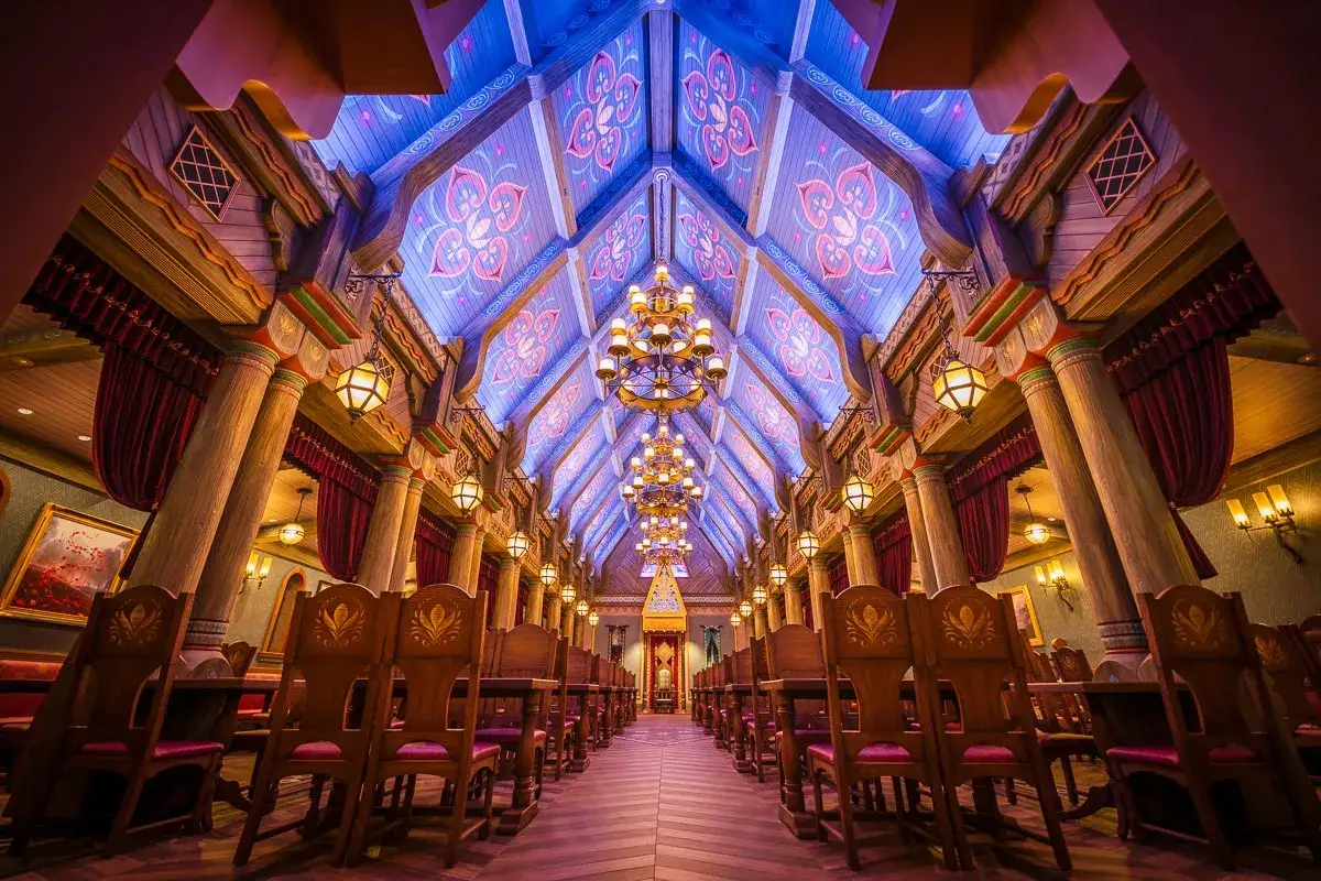 Ein prunkvoller Speisesaal im Stil von Frozen Disneyland, mit Holzsäulen, Kronleuchtern und einem blau-lila beleuchteten Dach mit Ornamenten.