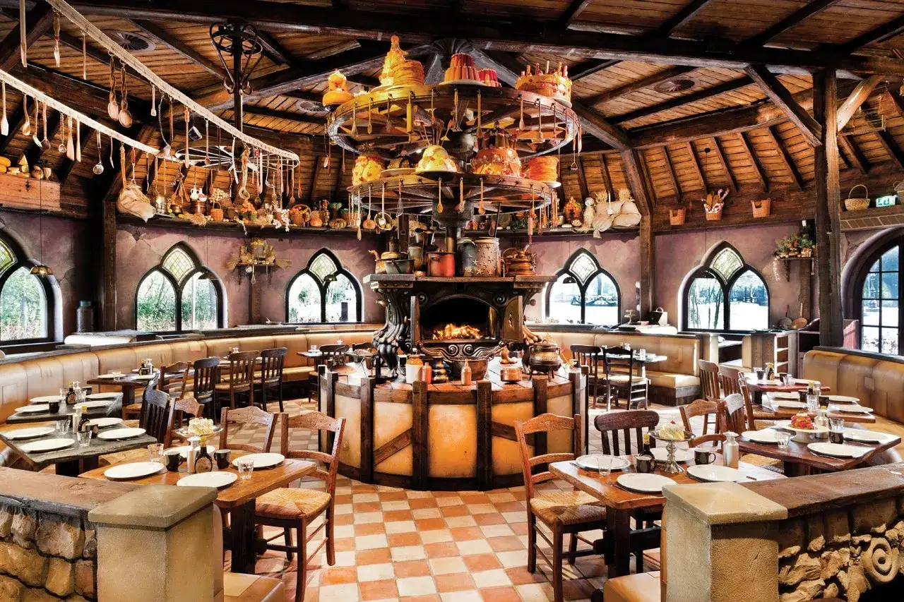 Gem&uuml;tliches Efteling Restaurant mit rustikalen Holztischen, Kamin und einer drehenden Kuchenpyramide.