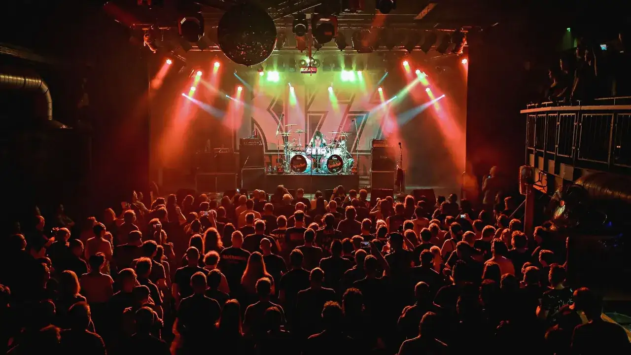 Konzert in der Zeche: Ein Schlagzeuger spielt vor jubelndem Publikum, beleuchtet von roten und grünen Scheinwerfern.