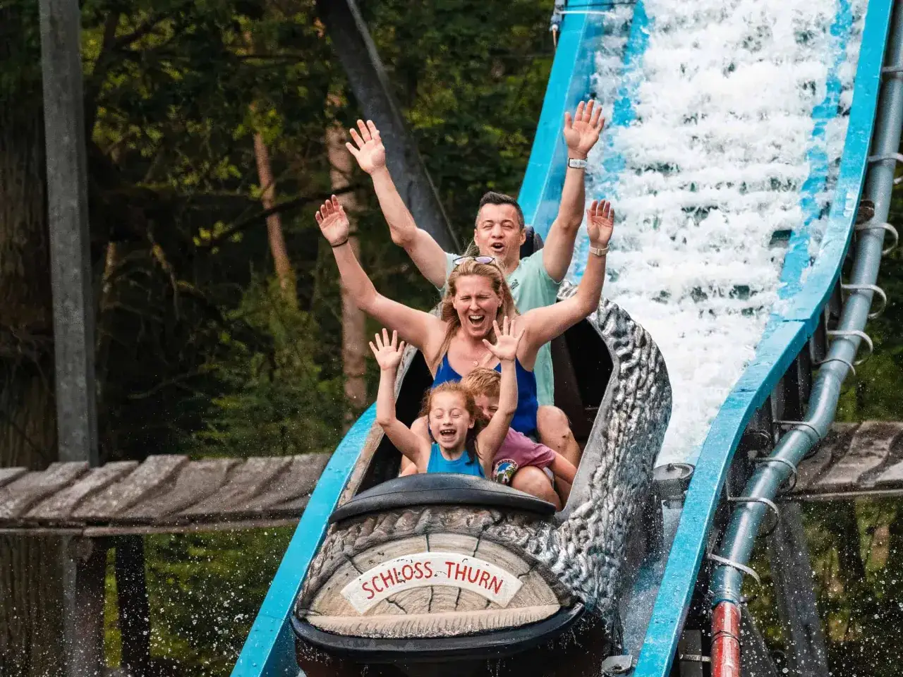 Familie hat Spaß auf einer wilden wasserbahn im Freizeitpark. Sie fahren mit einem Boot durch spritzendes Wasser und jubeln.