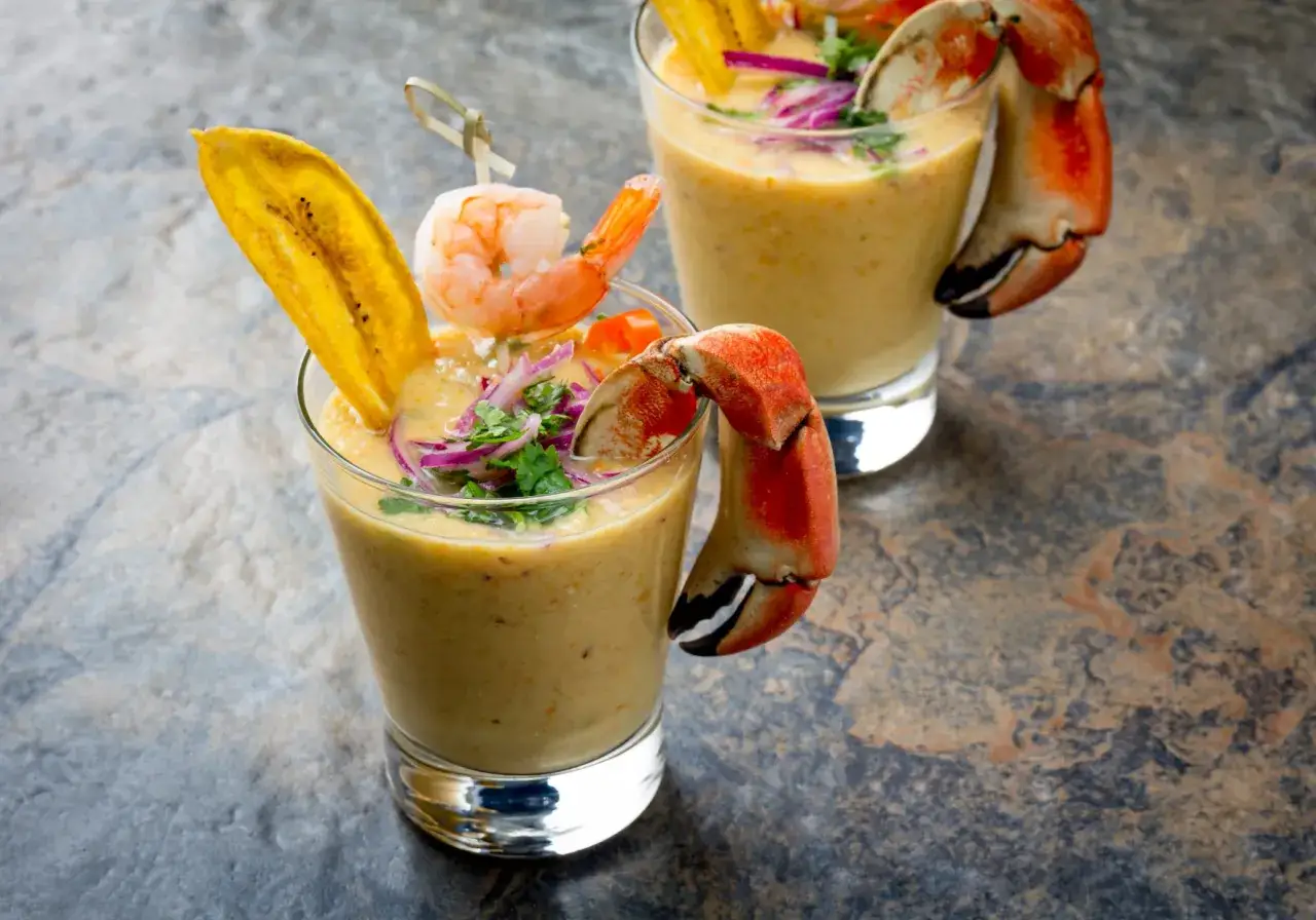 Zwei Gläser mit cremiger Tigermilch, garniert mit Garnelen, Bananenchips und Krabbenkrallen.